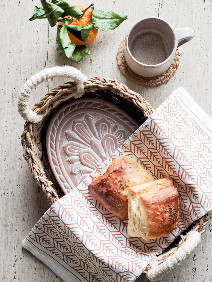 Terracotta plate engraved with a flower design into an oval basket is served with a hand screen printed tea towel.