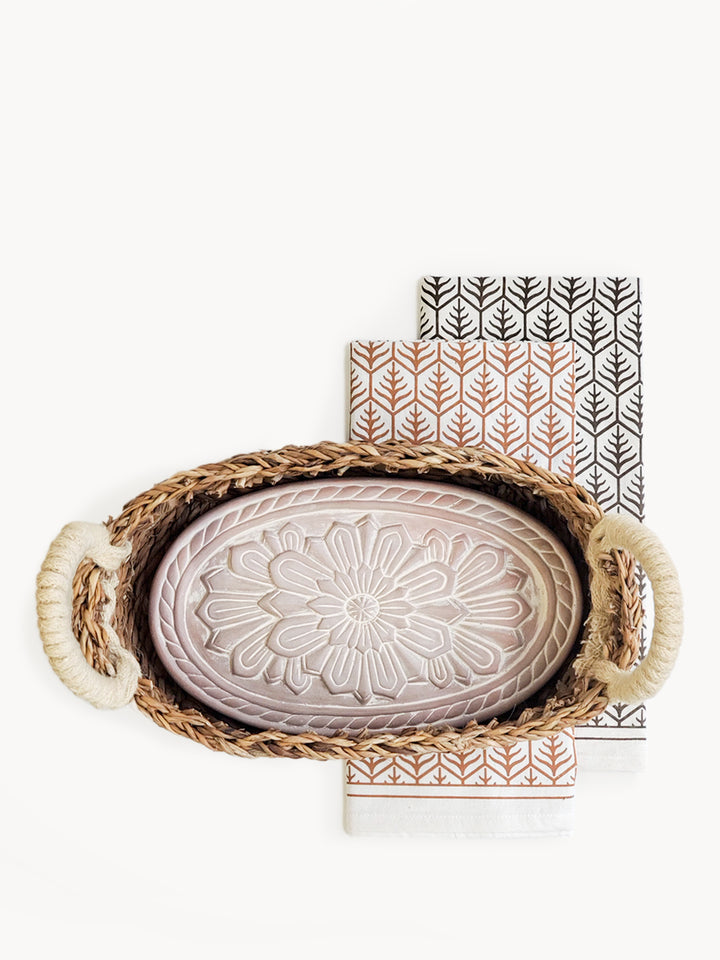 Terracotta plate engraved with a flower design into an oval basket with hand screen-printed tea towels in two colors on natural cotton