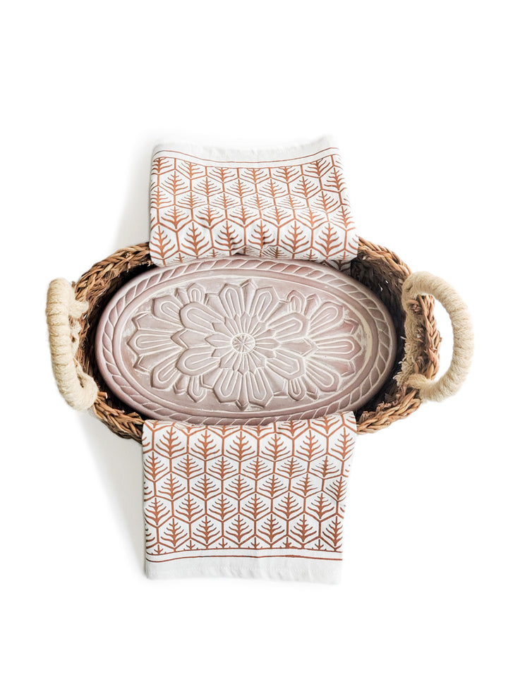 Terracotta plate engraved with a flower design into an oval basket with a light brown hand screen printed tea towel.