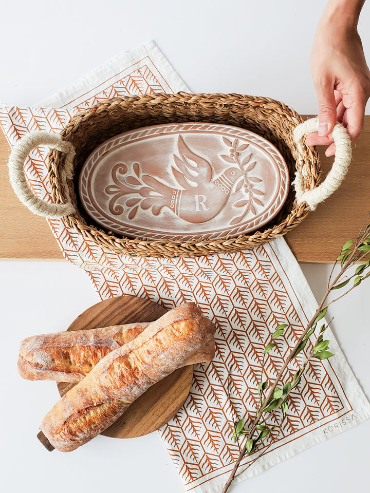 Hand engraved terracotta plate with a bird & leaf design into an oval basket and hand screen-printed tea towel on natural cotton 