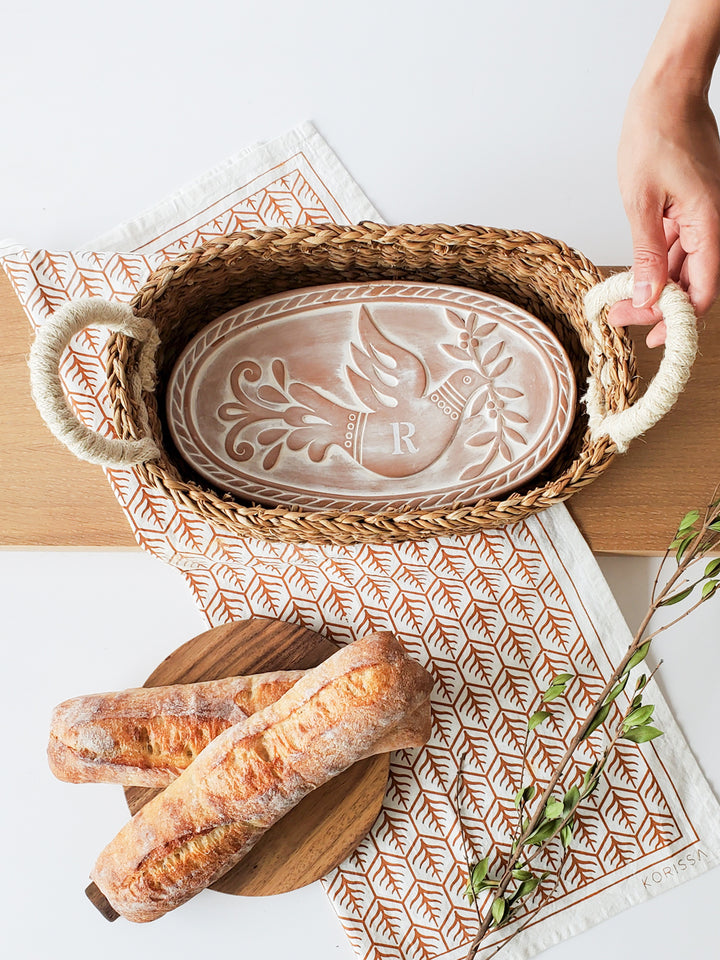 Hand engraved terracotta bread warmer with a bird & leaf design into an oval basket and hand screen printed tea towel printed on natural cotton 