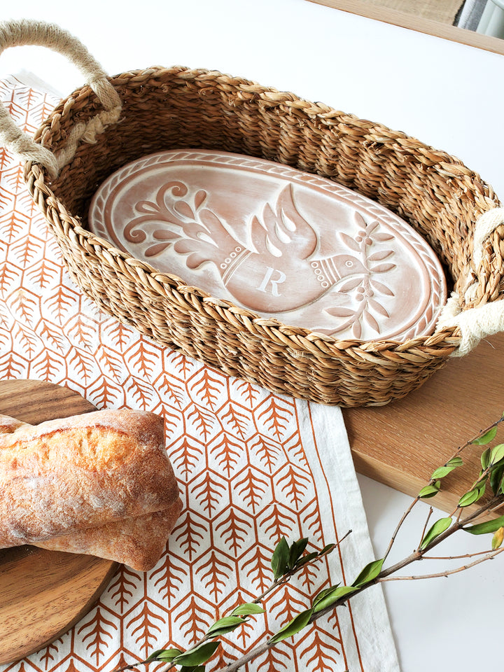 Hand engraved terracotta bread warmer with a bird & leaf design into an oval basket and hand screen printed tea towel printed on natural cotton