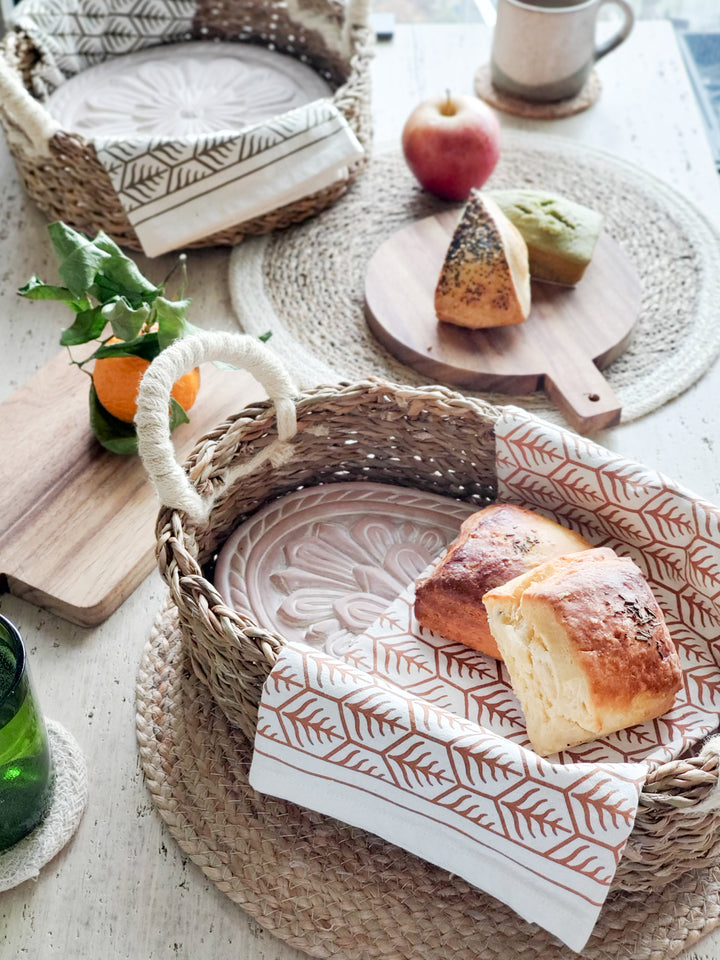 Terracotta plates engraved with a flower design into an oval and a round basket, hand screen-printed tea towels printed in two colors on natural cotton, Wooden serving boards, Savar placemat, Kata placemat and coasters