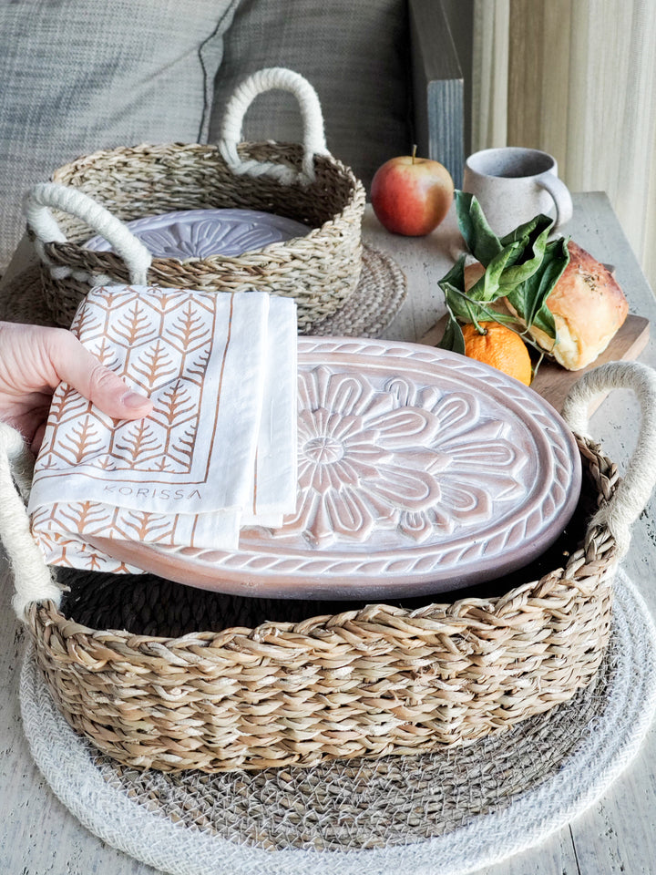 Terracotta plate engraved with a flower design into an oval, a round basket is served with hand screen-printed tea towels in two colors on natural cotton